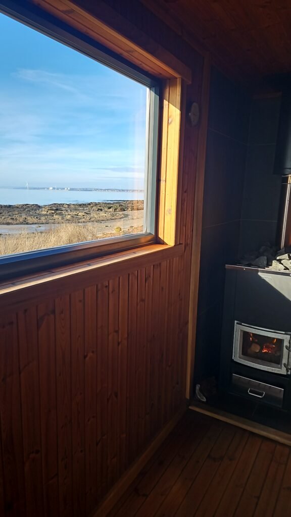 Interior of Largo Castaway Sauna with wood-fired stove and window view of Largo Beach.