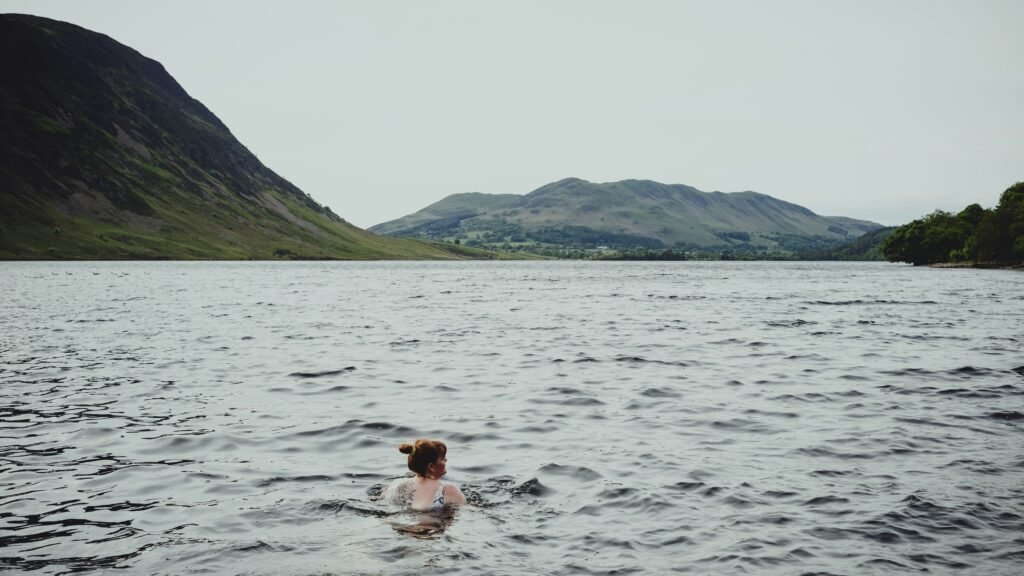 Person swimming in a cold loch surrounded by hills as part of a wild sauna experience