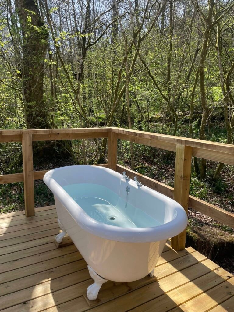 Cold plunge bath on wooden deck beside outdoor sauna in woodland setting