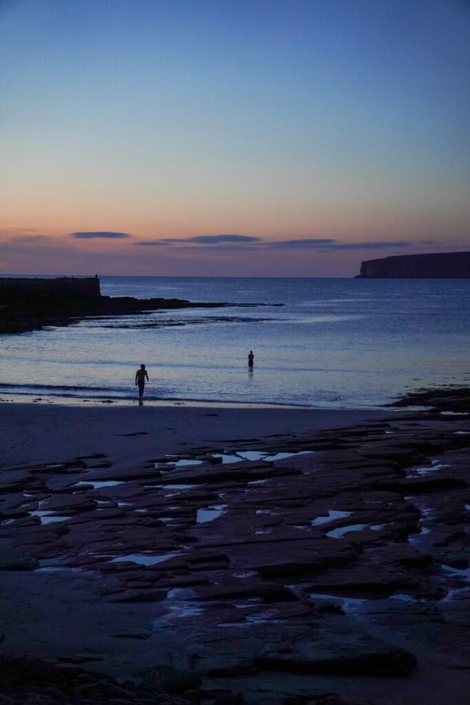 People entering the sea at dusk beside sauna for cold water immersion