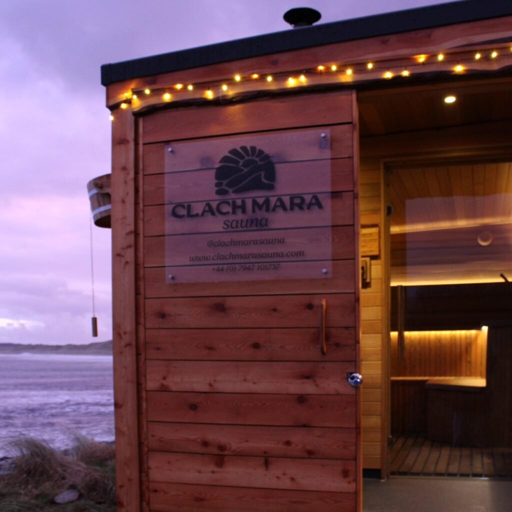 Exterior of Clach Mara sauna glowing with warm lights at night by the sea