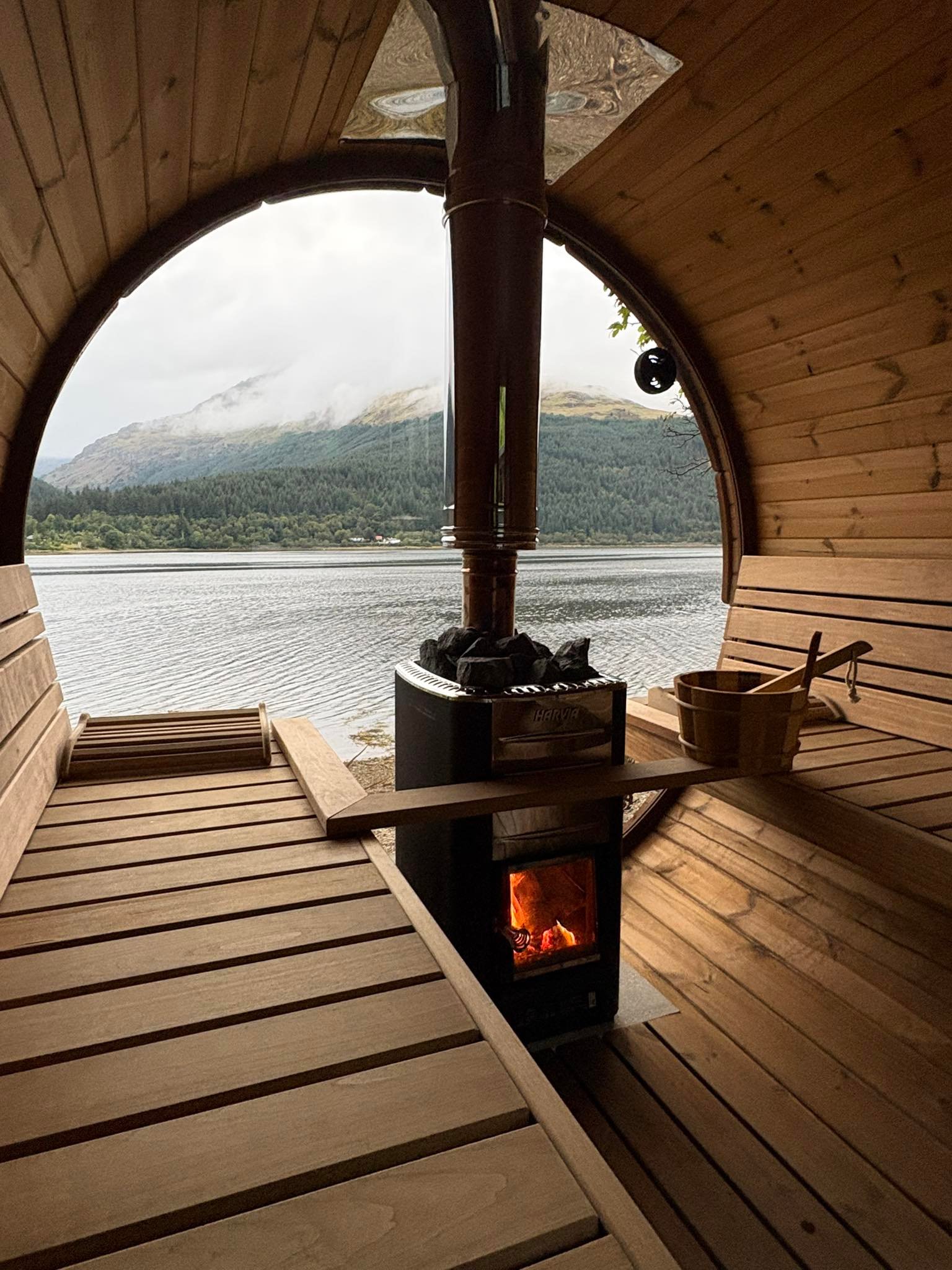 Interior of Eir Sauna’s wood-fired barrel sauna overlooking Loch Long through a circular window