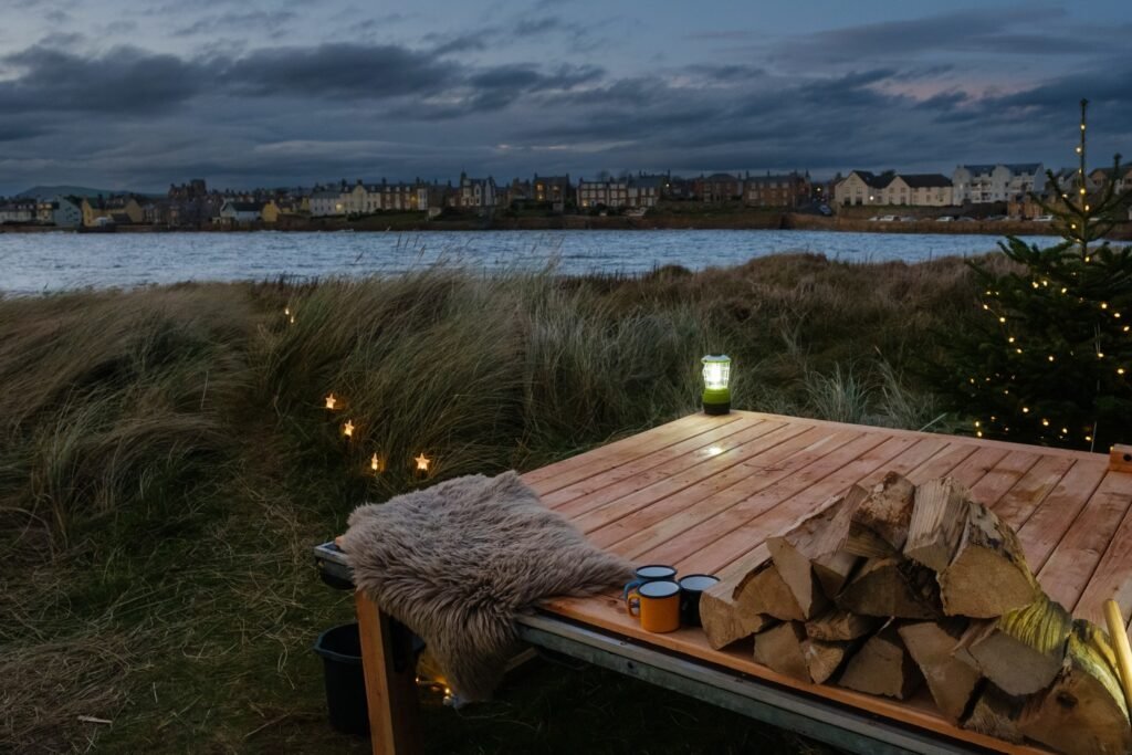 Wooden deck with firewood and mugs outside Elie Seaside Sauna at dusk in Fife