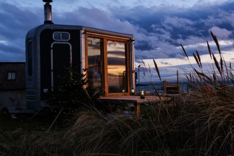 Elie Seaside Sauna glowing at dusk beside coastal grass and sea in Fife, Scotland