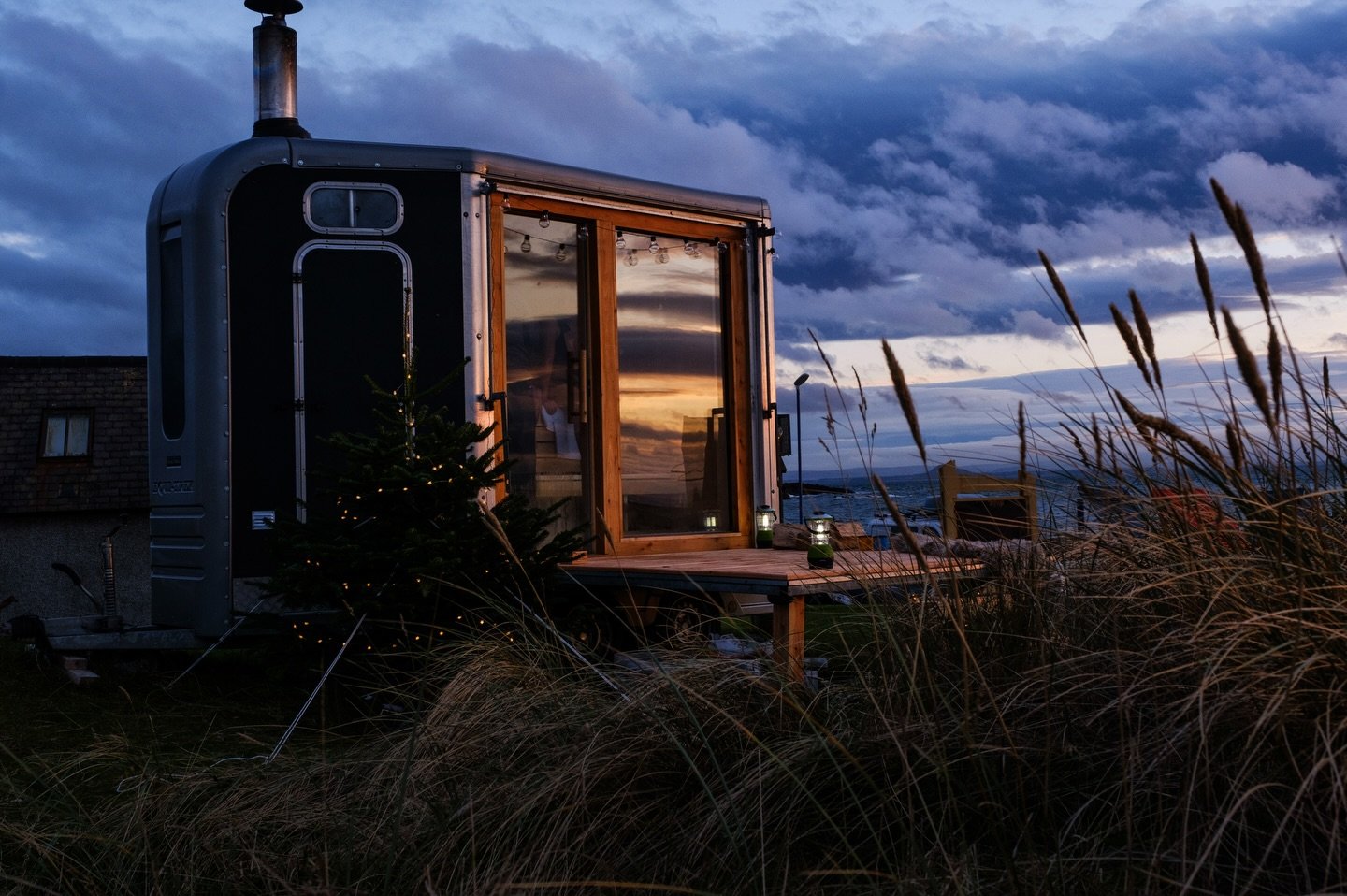 Elie Seaside Sauna glowing at dusk beside coastal grass and sea in Fife, Scotland