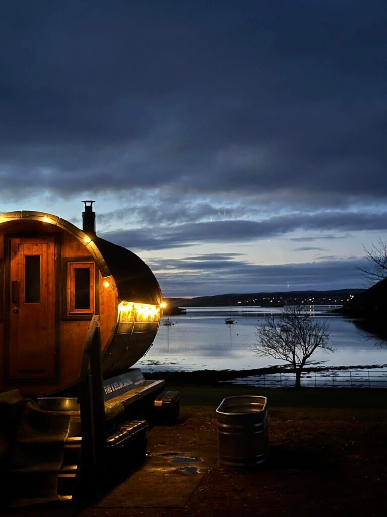 Wood-fired sauna lit at dusk overlooking the water at Shieldaig Lodge near Gairloch