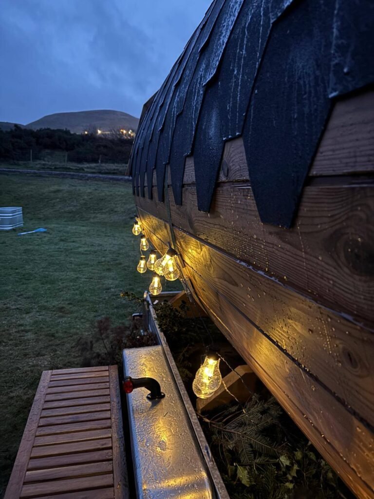 Evening view of Pentland View Outdoor Sauna with lights on and hillside backdrop in Edinburgh