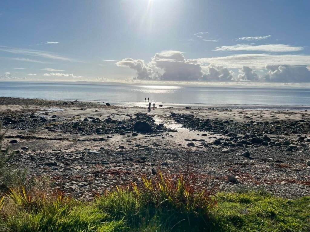People walking into the sea from the beach at Whiting Bay with calm coastal views