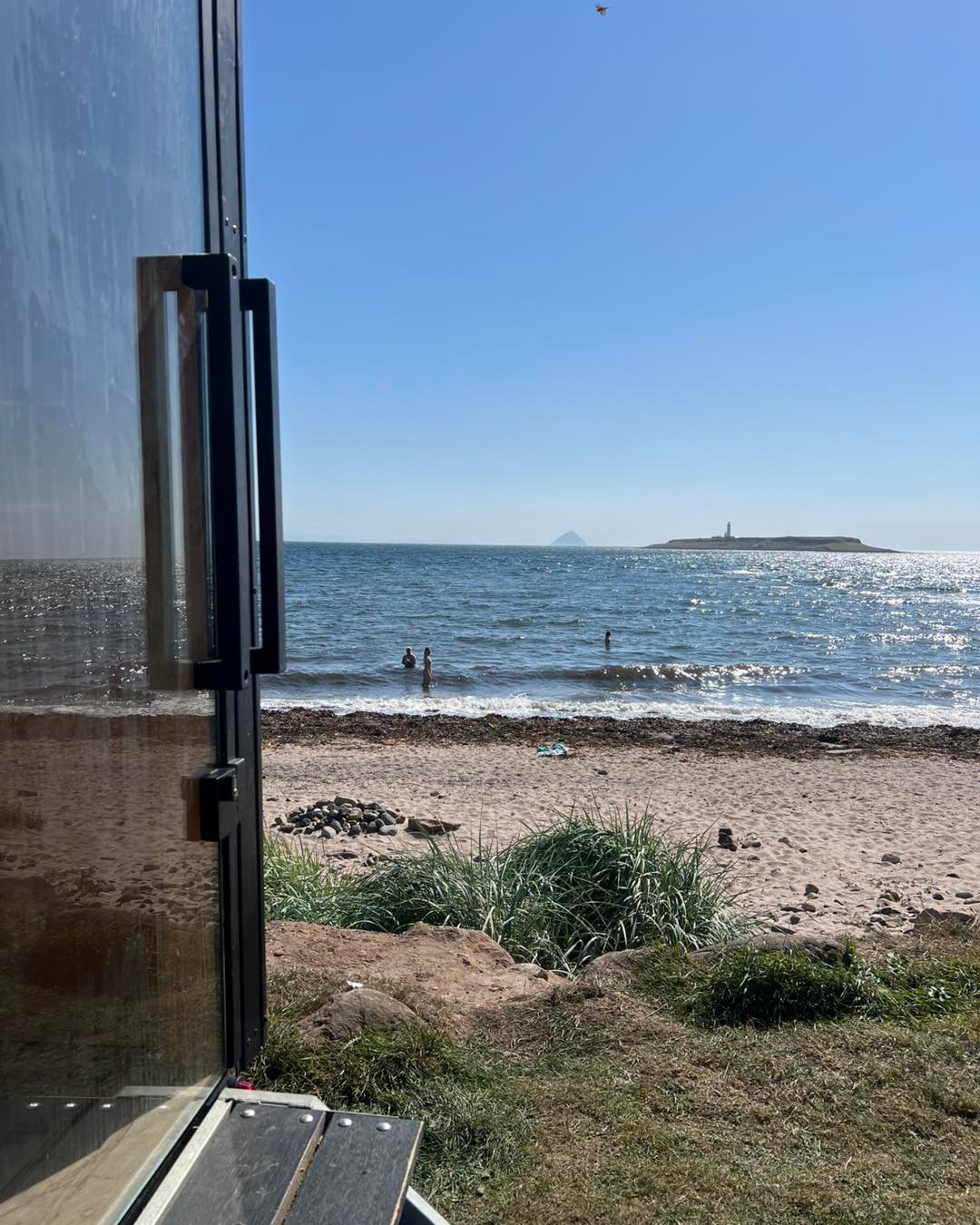 View from the sauna doorway across Whiting Bay with people sea swimming