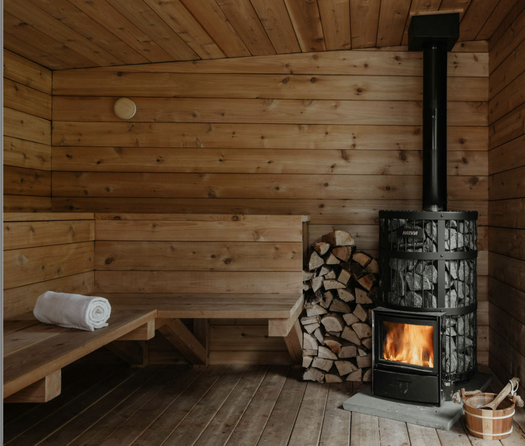 Interior of a wood-fired outdoor sauna with tiered wooden benches and sauna heater stones