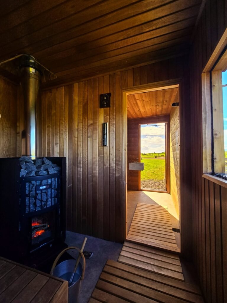 Inside BYRE at Balgone sauna showing wood-fired Harvia stove with open door looking out to East Lothian countryside