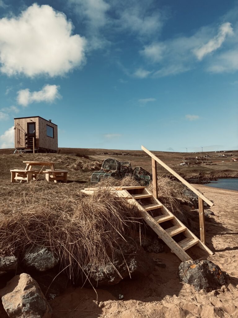 Nordic Glow Shetland Hot Hoose sauna on the hillside with wooden steps and picnic bench at Ollaberry Bay