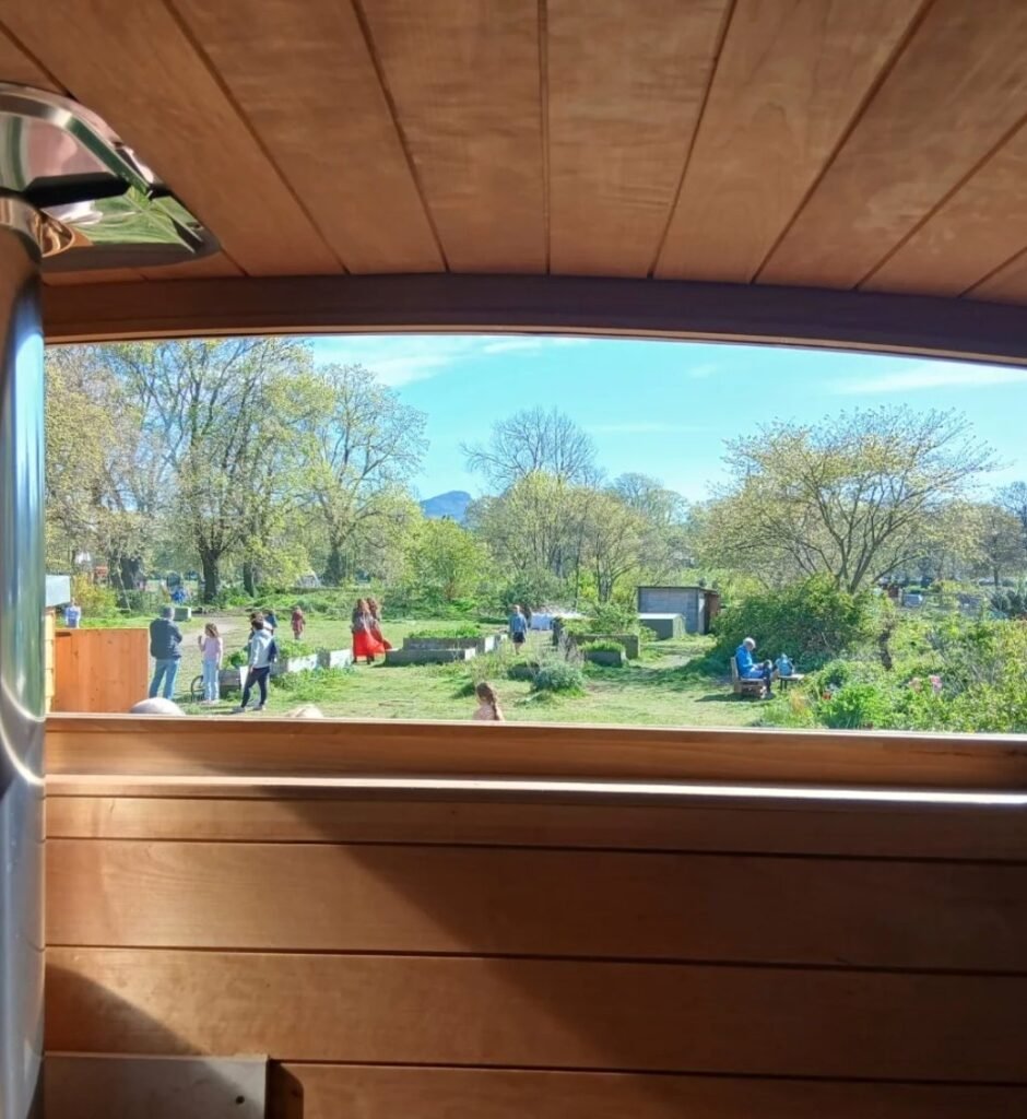 View from inside Puffin Sauna Leith looking out over Leith Community Croft with Arthur's Seat in the distance
