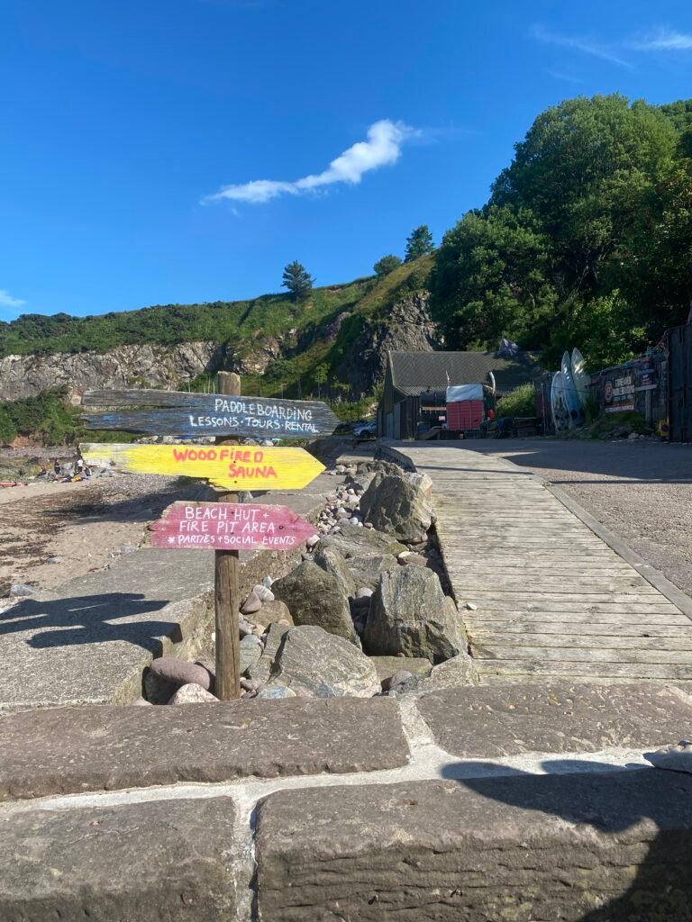 Hand painted reclaimed wood signs for the wood fired sauna and firepit area, beach and sea in the background