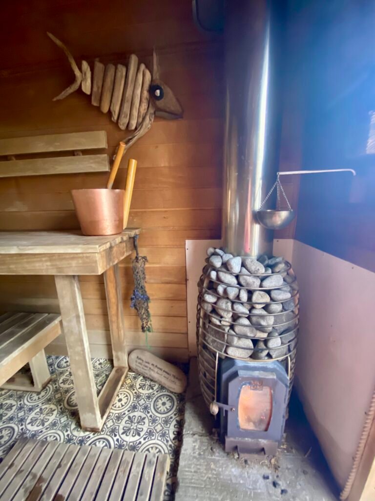 Close up of the wood fired stove, bucket, ladle and hanging essential oil bowl inside Driftwood Sauna