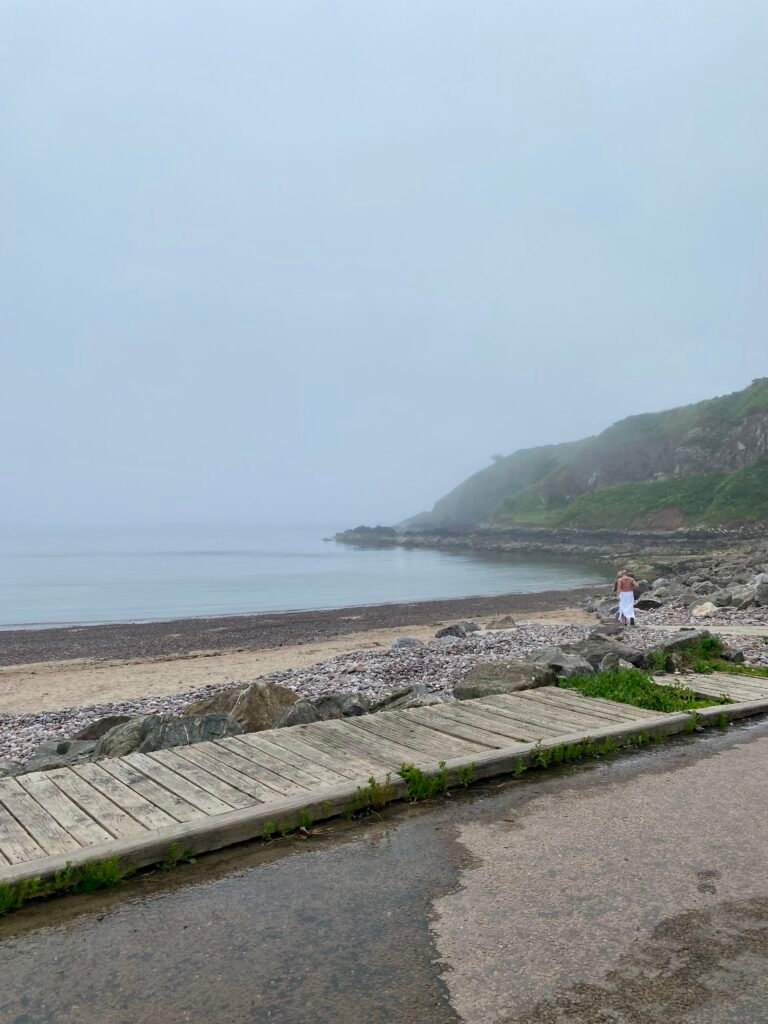 A lone figure walking across an empty beach towards the sea near Driftwood Sauna, Stonehaven