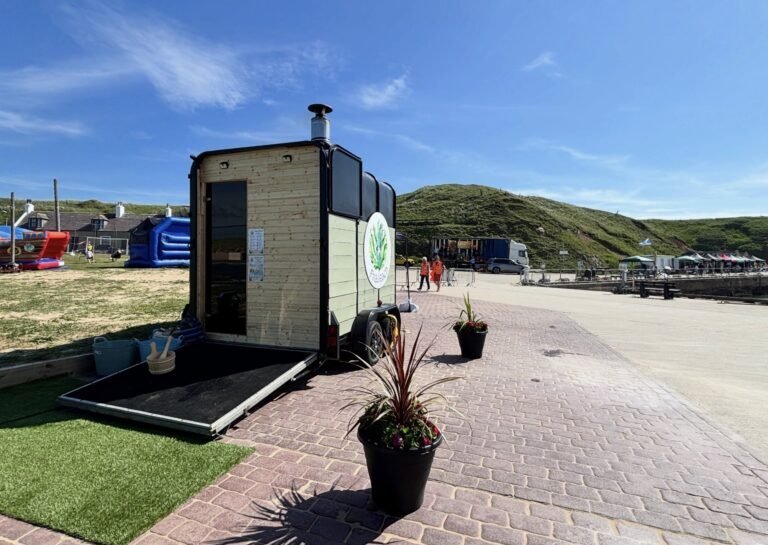 Fraileach Sauna Cruden Bay trailer sauna exterior with branded door open, Cruden Bay harbourfront behind