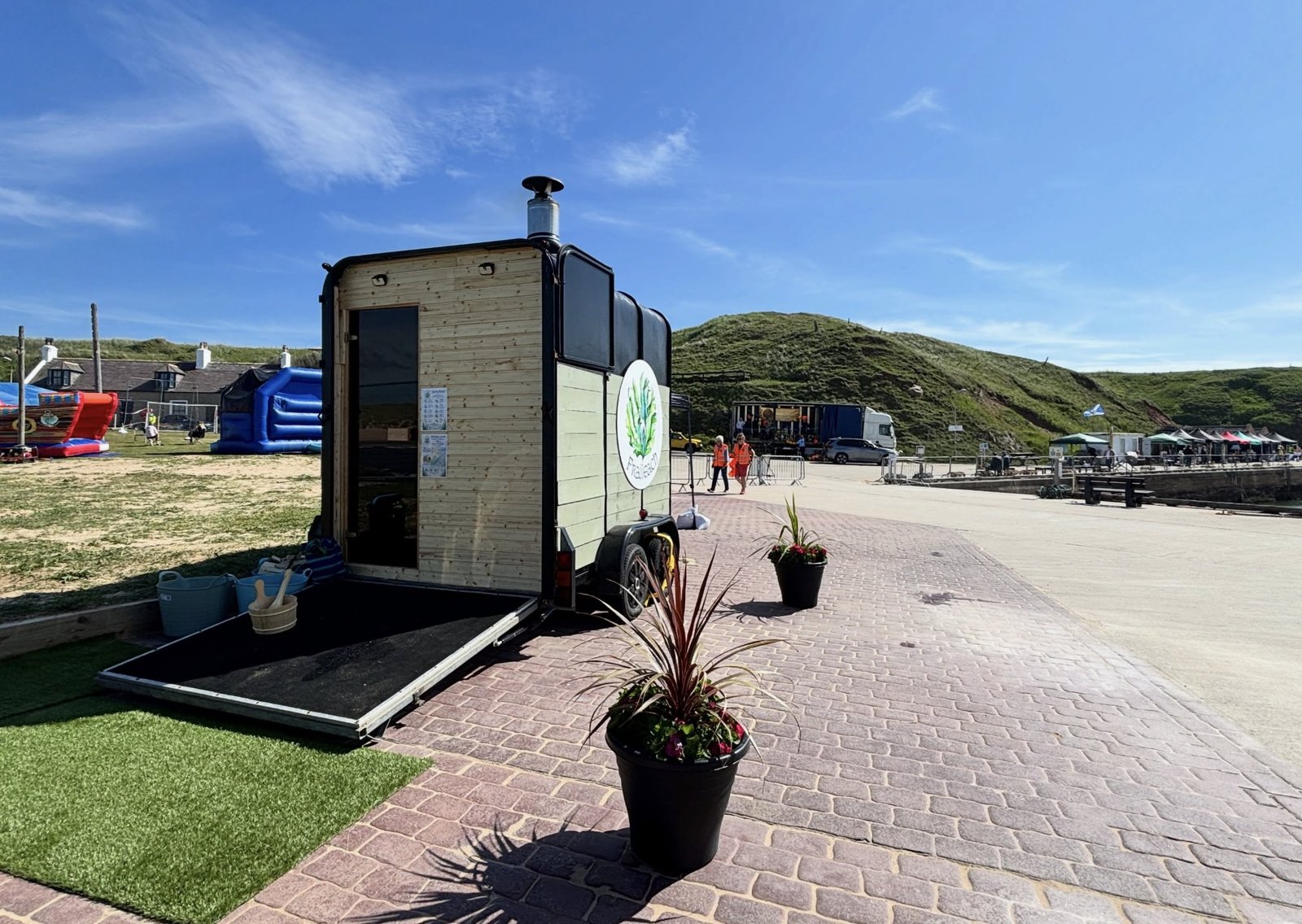 Fraileach Sauna Cruden Bay trailer sauna exterior with branded door open, Cruden Bay harbourfront behind