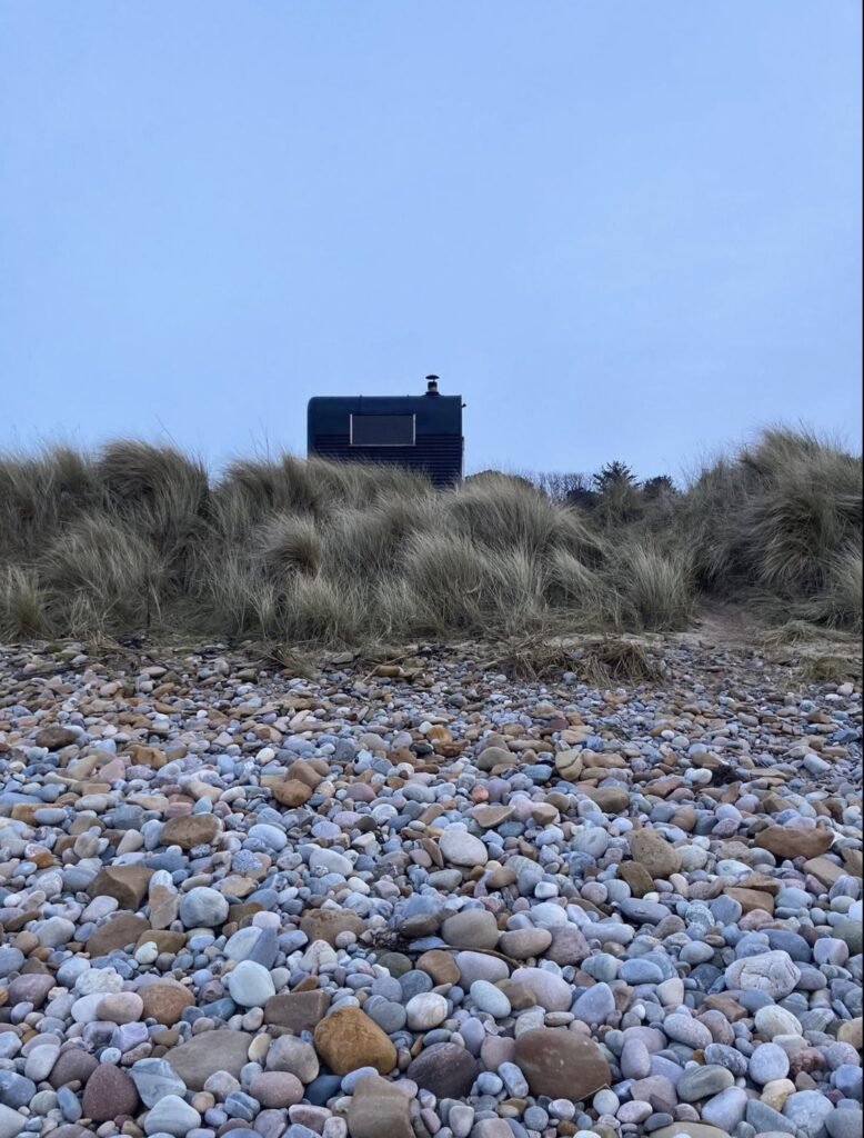 Fyrhus Sauna Hopeman silhouetted above the pebble beach at dusk