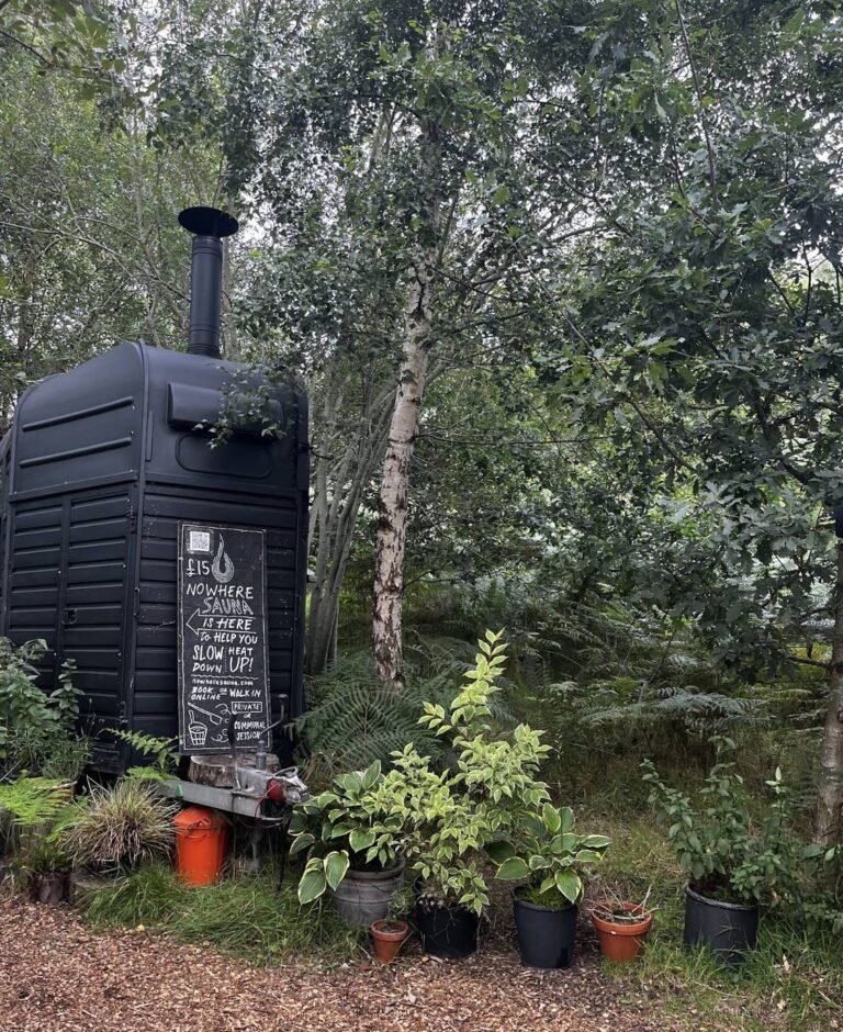 Nowhere Sauna Comrie Croft exterior tucked in the woodland with its chalkboard sign