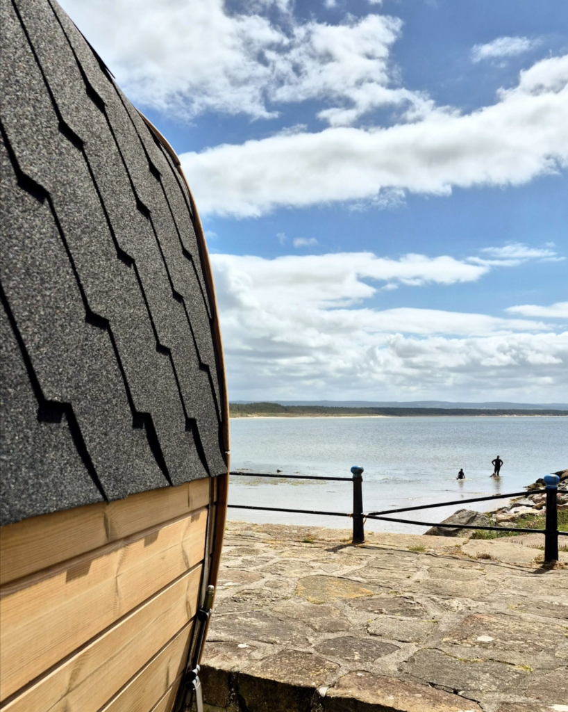 Orka Sauna, Burghead: the shingled roof of the barrel sauna, with swimmers in the bay behind