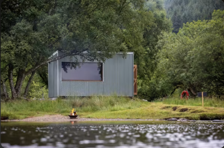 Rvival Sauna beside Loch Voil, with its large window and a fire pit on the shore