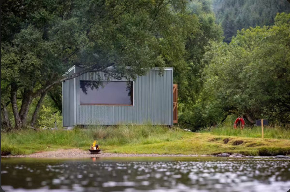 Rvival Sauna beside Loch Voil, with its large window and a fire pit on the shore