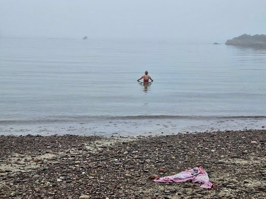 Wading into the sea near Driftwood Sauna, with a towel left on the pebble beach