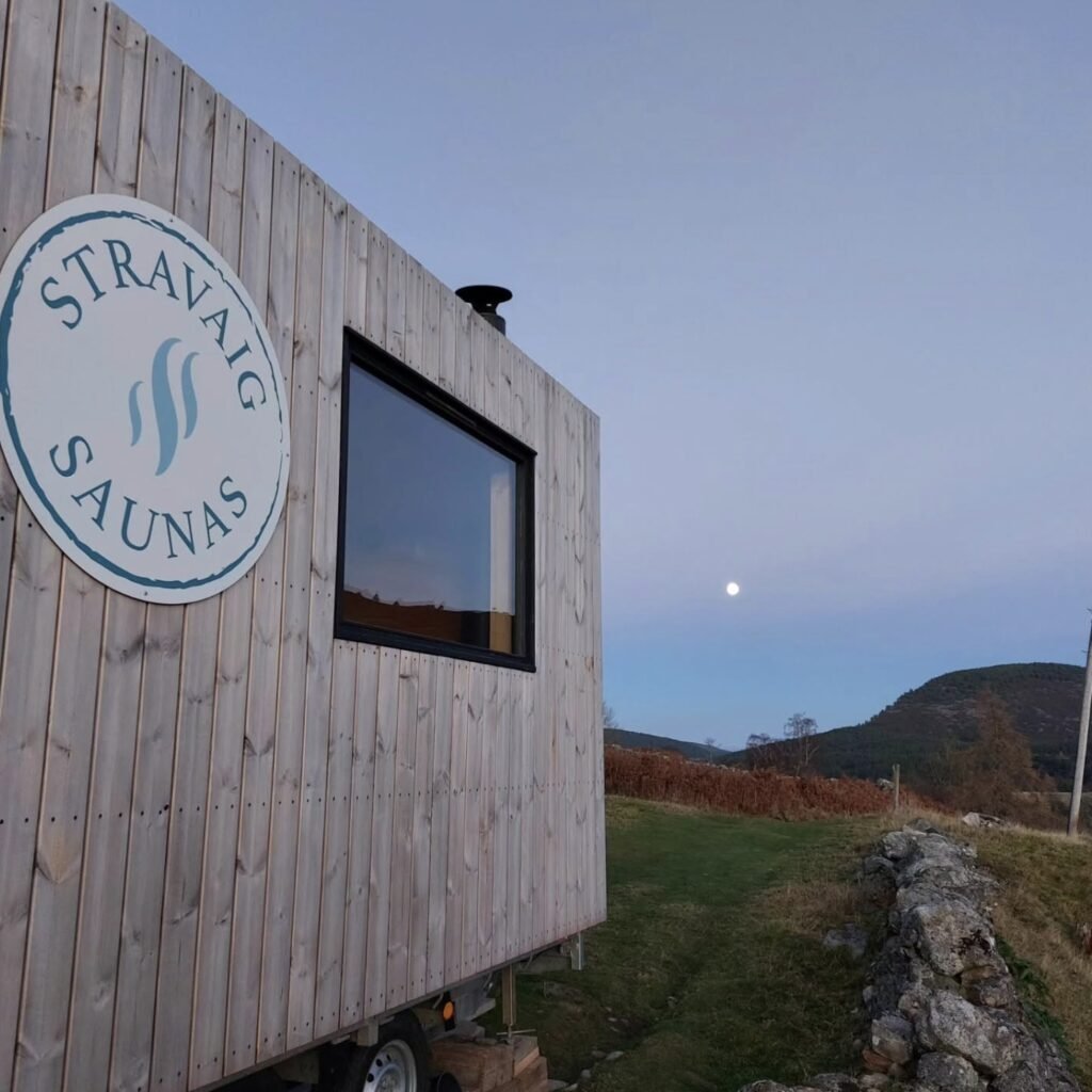 Stravaig Sauna Crathie branded sign at dusk with the moon over the Cairngorms