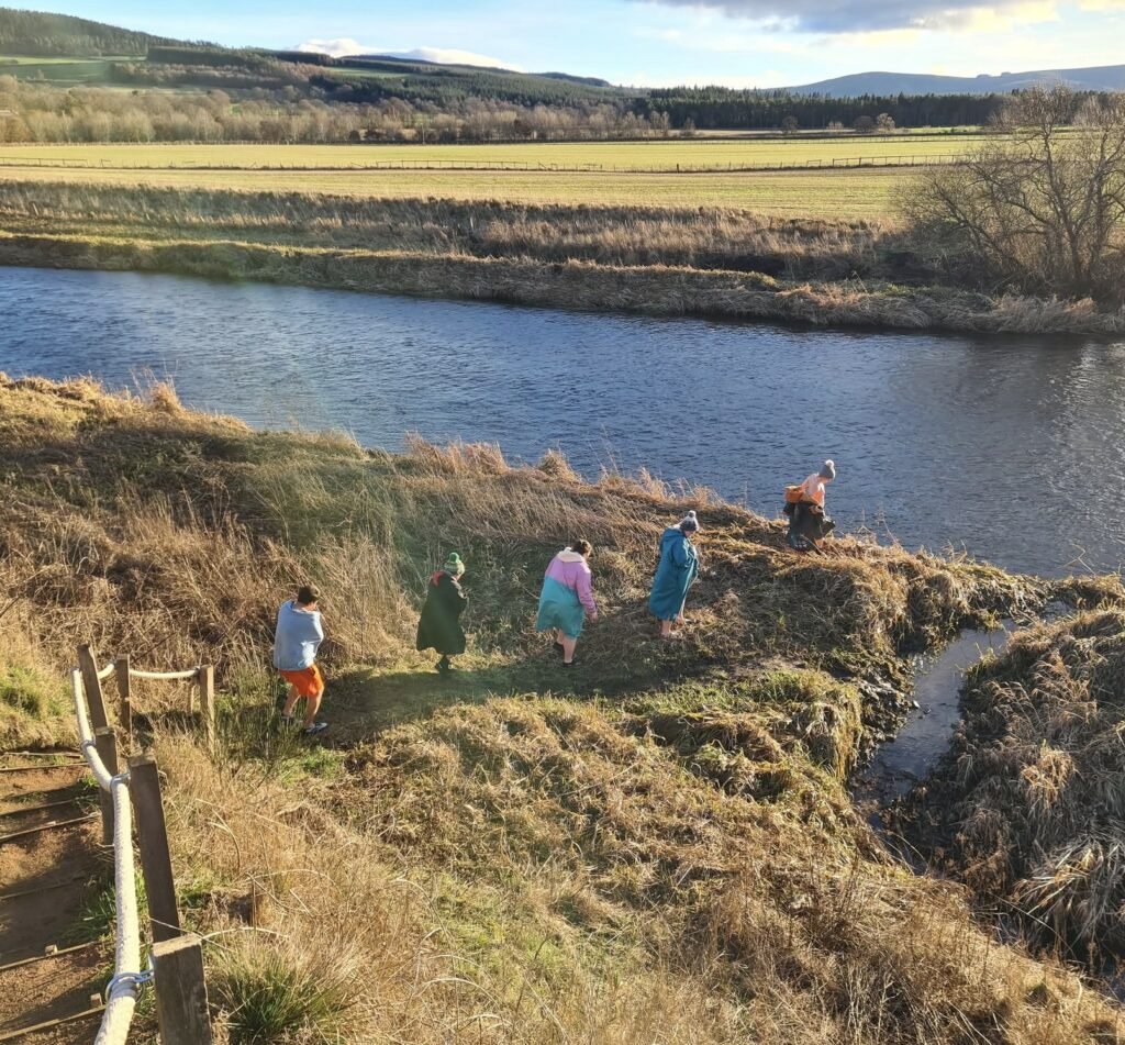 The Little Sauna Keig group in robes walking along the riverbank