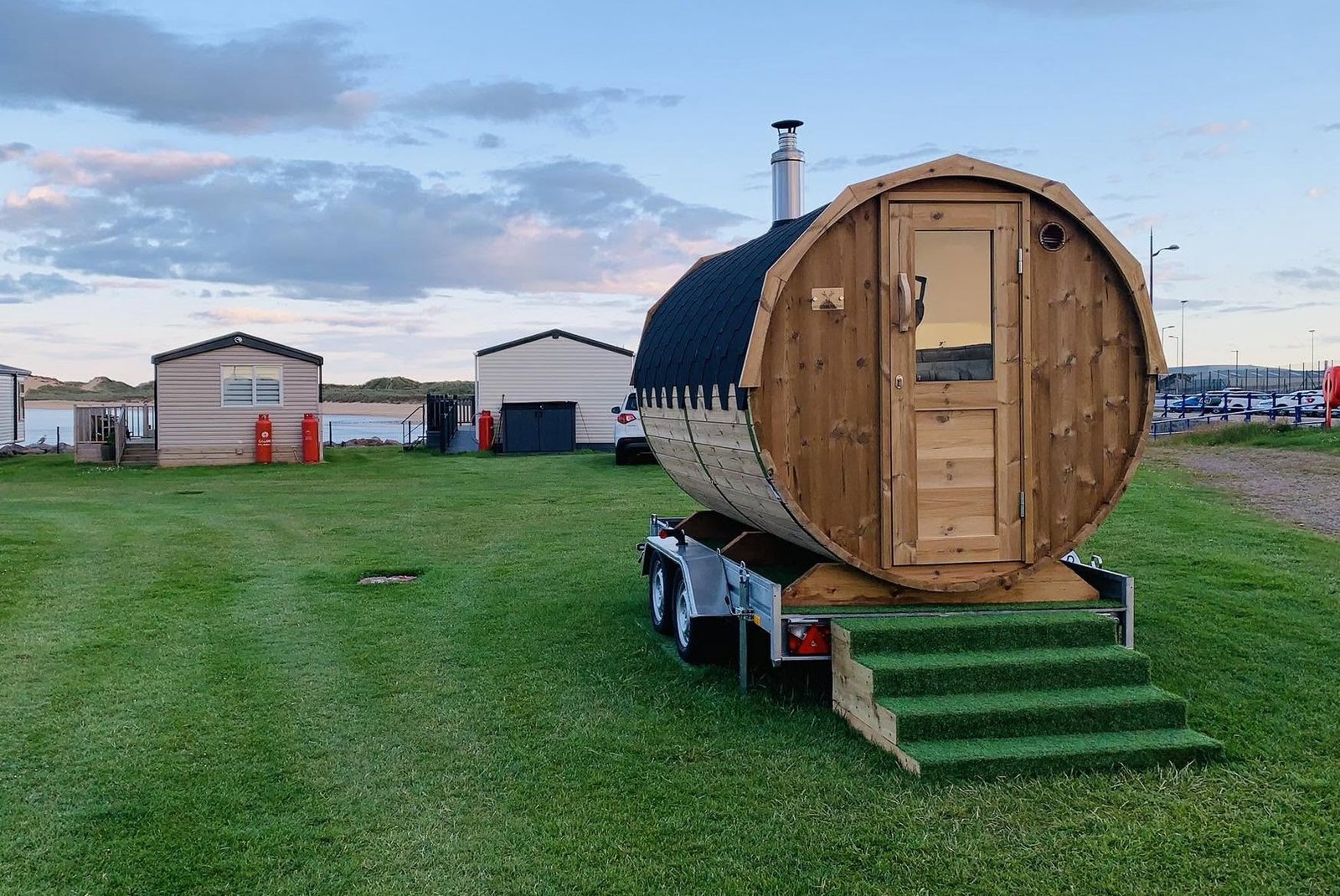 The Sauna Hoose Fraserburgh barrel sauna on its trailer at golden hour, dunes and caravan park behind