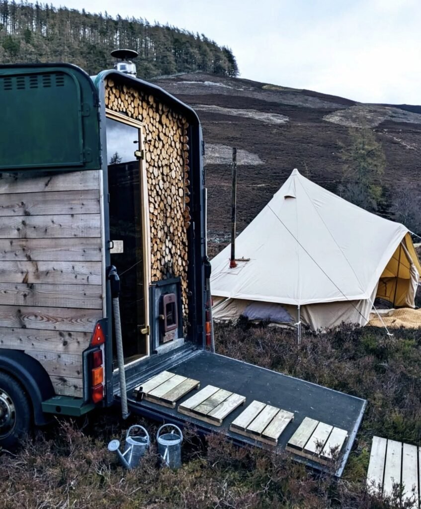 Wild Braemar Wilderness Sauna Cairngorms entrance with stacked firewood and bell tent behind