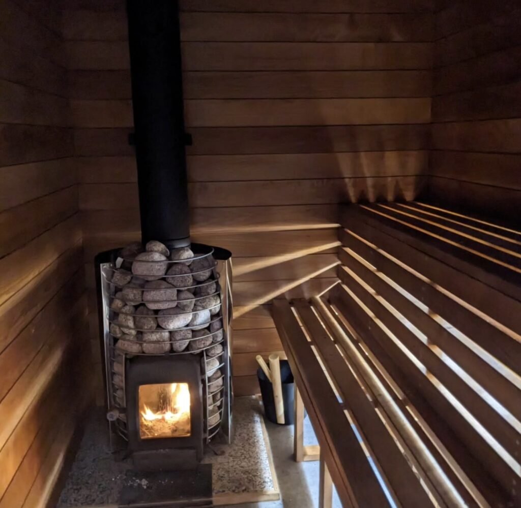 Wild Braemar Wilderness Sauna Cairngorms interior with wood-fired stove lit and river stone heater