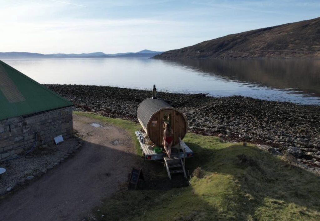 Applecross Sauna Wester Ross aerial view of the barrel sauna on its trailer between the boatshed and the rocky shore