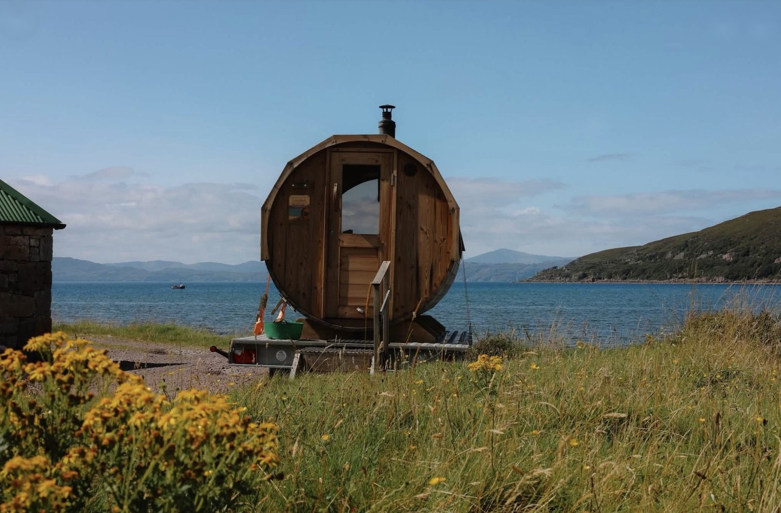 Applecross Sauna Wester Ross wood-fired barrel sauna on a trailer beside Applecross Bay with yellow ragwort in the foreground