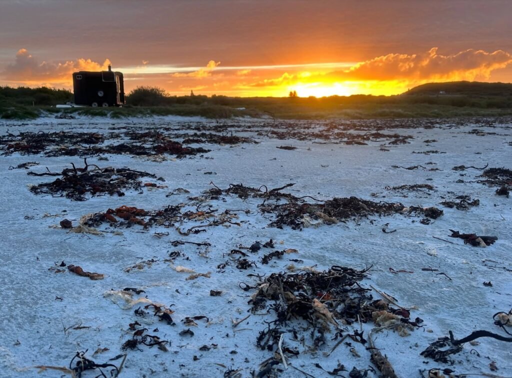 Bothan Jura Wild Sauna Isle of Jura sauna silhouetted against an orange sunset over the beach