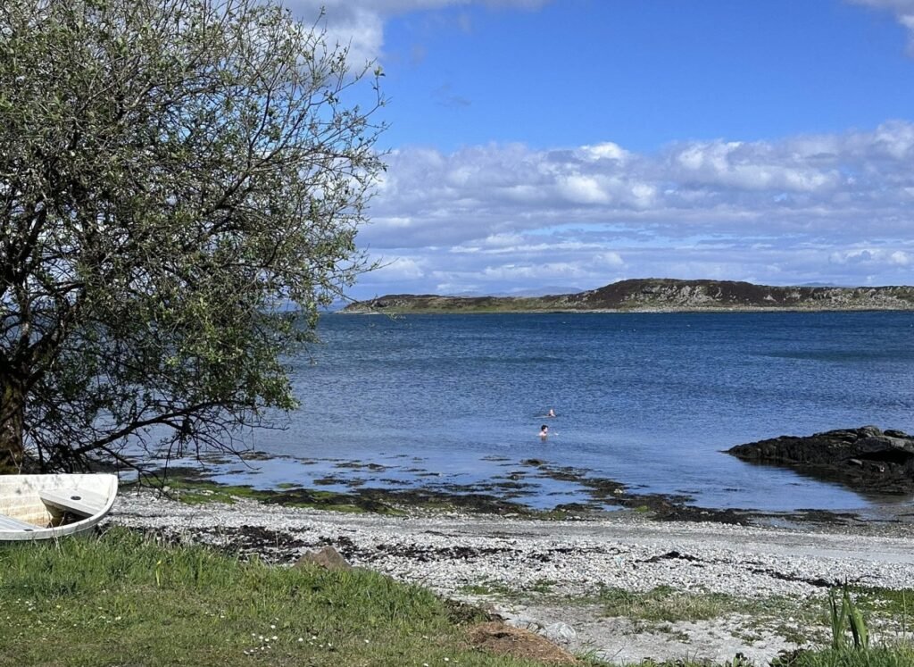 Bothan Jura Wild Sauna Isle of Jura sea swimmers in the bay beside a pebble beach and a pulled-up rowing boat