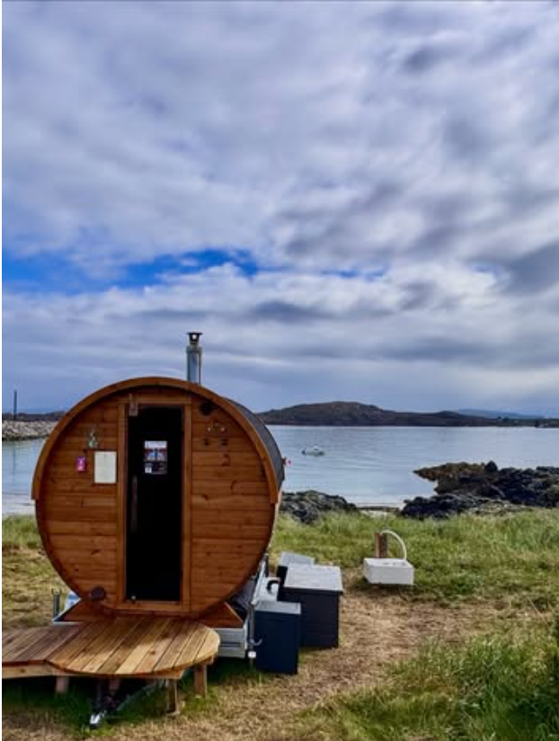 Iona Hotbox Sauna Isle of Iona barrel sauna on the grass beside the shore with rocks and calm water behind