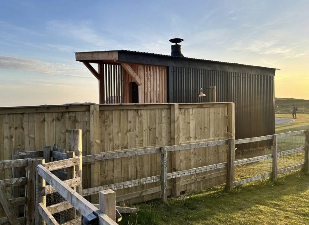Loyly Sauna Clachtoll sauna cabin and outdoor shower in the golden evening light behind a timber fence