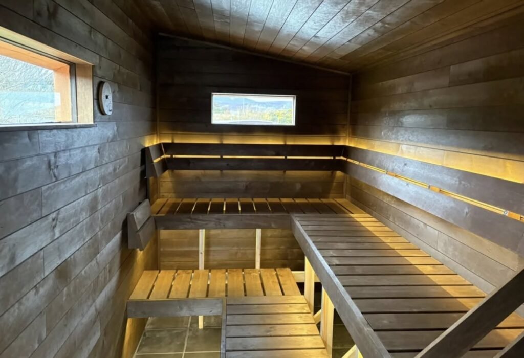 Loyly Sauna Clachtoll dark-stained timber sauna interior with tiered benches, warm LED lighting and windows to the outside