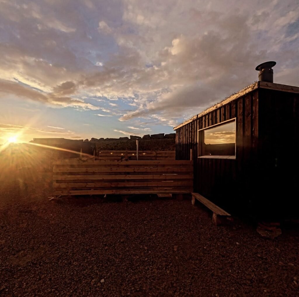 Seaview Sauna Dunnet Bay black timber sauna with a window reflecting the setting sun over the gravel terrace